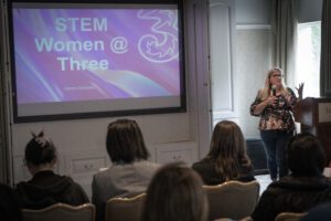 A speaker standing in front of an audience holding a microphone